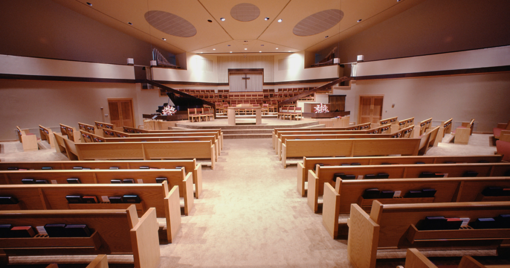 Worship center filled with pews facing the front of a church with a cross in the front