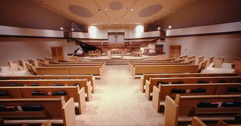 Worship center filled with pews facing the front of a church with a cross in the front