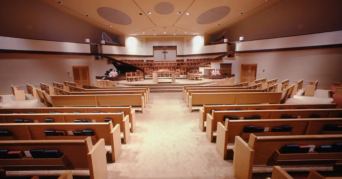 Worship center filled with pews facing the front of a church with a cross in the front