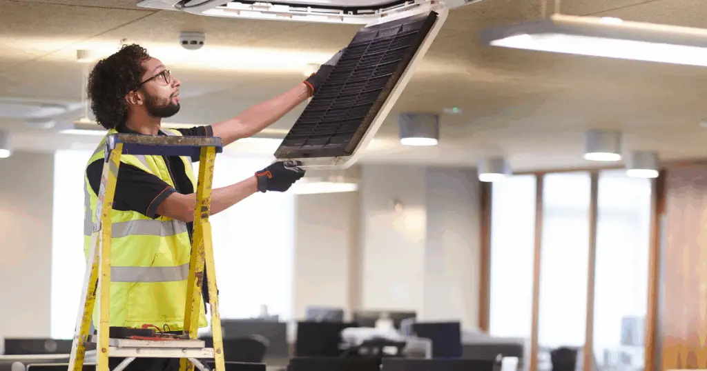 Facility worker changing the filter of an HVAC unit in the ceiling.